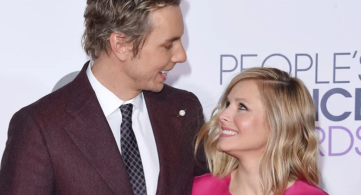 Couple smiling at each other on the red carpet, dressed in formal attire, with "People's Choice Awards" logo in background.