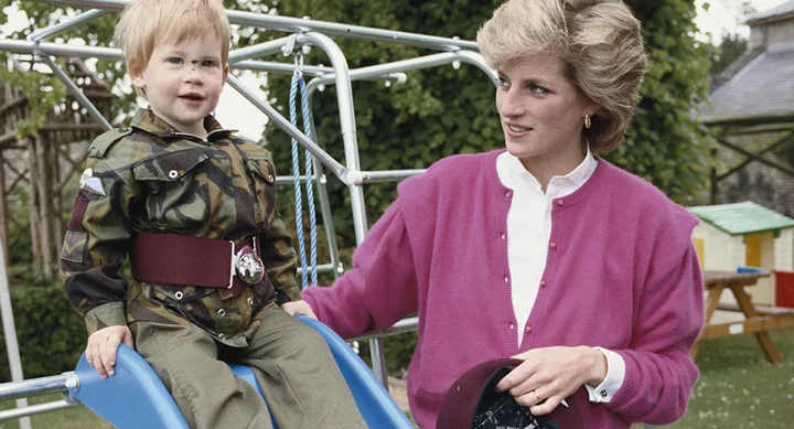 A woman in a pink sweater with a young child in a camouflage outfit on a playground slide.