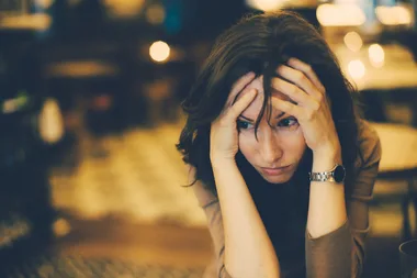 A woman with hands on her head, looking distressed in a softly lit environment.