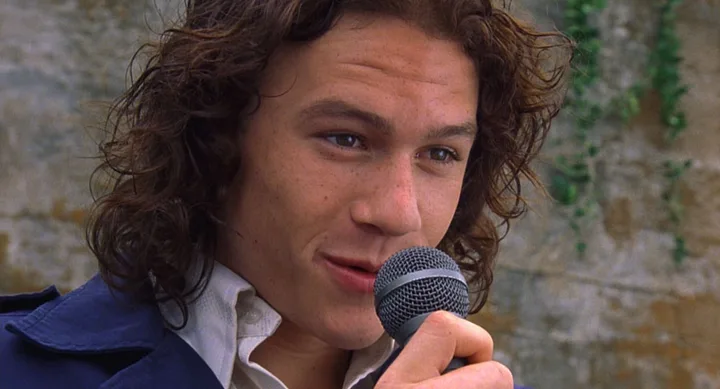 Person with curly hair sings into a microphone outdoors.