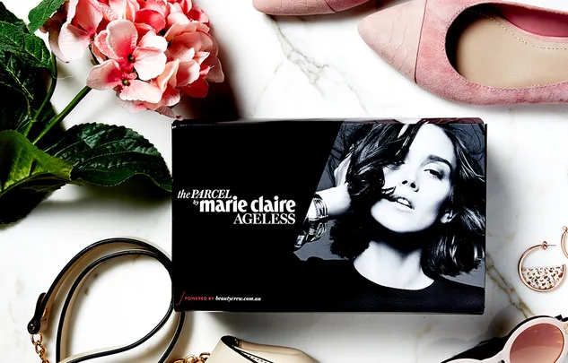 Box labeled "the Parcel by Marie Claire Ageless" with flowers, shoes, and accessories on a marble surface.