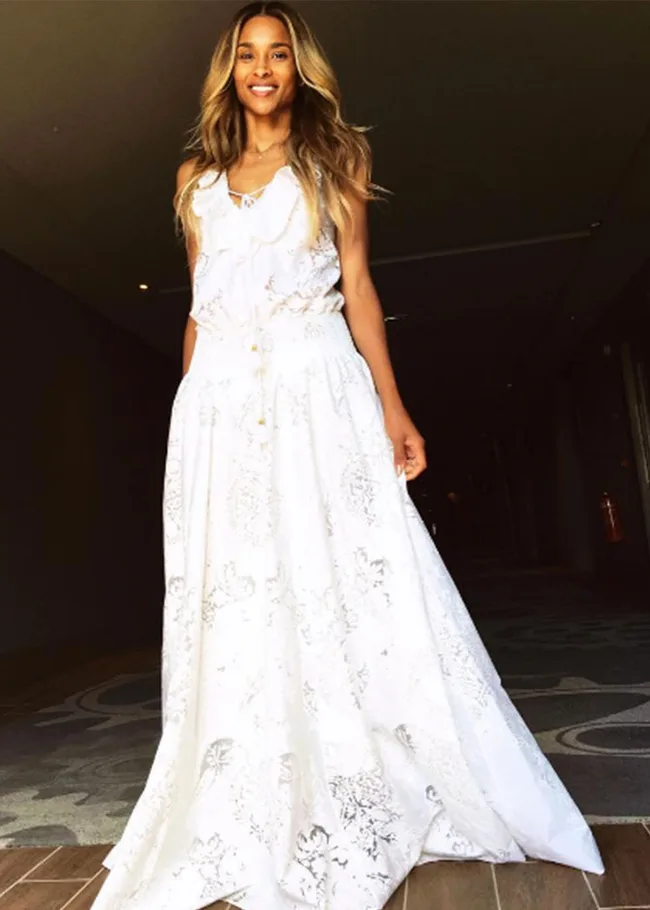 Woman in a white sleeveless dress with long wavy hair, standing indoors.