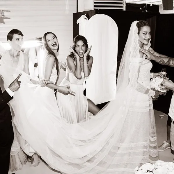 Bride in a wedding dress with veil, surrounded by bridesmaids holding the dress, all posing and smiling.