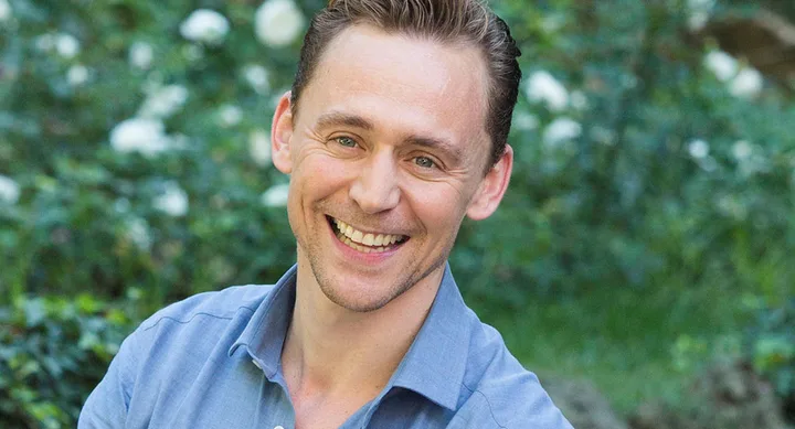 Smiling man in a blue shirt, outdoors with blurred green background.