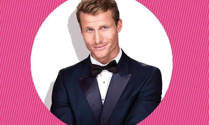 Man in a dark tuxedo and bow tie smiling against a pink and white striped background.