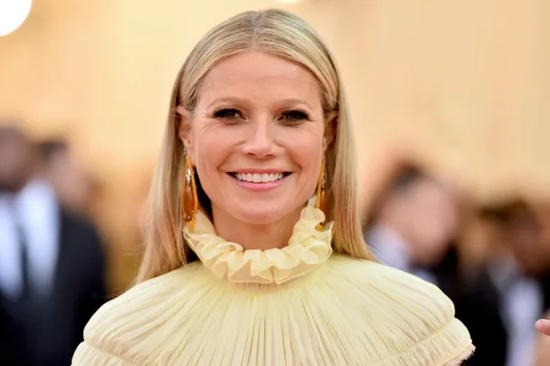 Woman in a yellow ruffled dress with long blonde hair, smiling at a formal event.