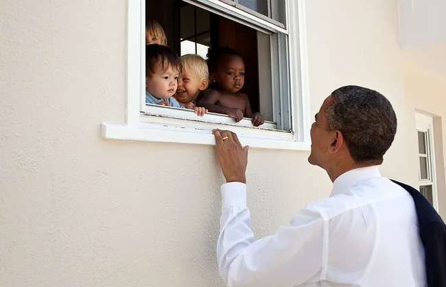 A man engaging with four children peeking from a window, smiling and interacting warmly.