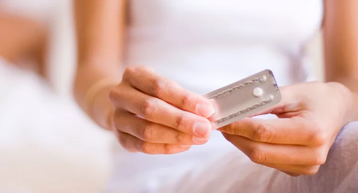 Individual holding a blister pack with two white tablets in a relaxed setting.