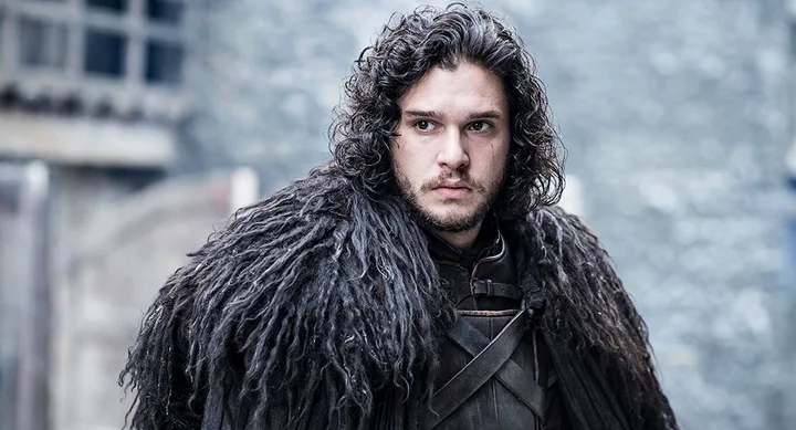 Young man with long dark hair and fur cloak in a medieval setting, appearing determined.