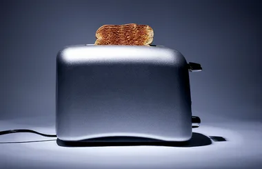 Silver toaster with a slice of toasted bread popping up against a dark background.