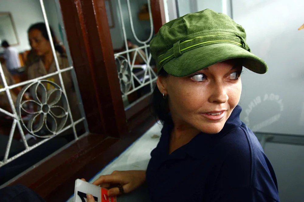 Woman in a green cap looking to her right inside a room with a decorative window grille.