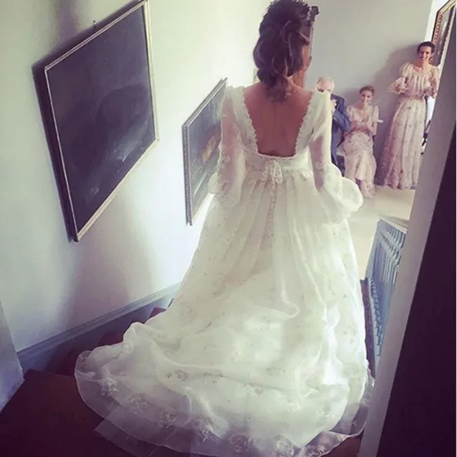 A woman in a long, white bridal gown descends stairs, with three people in formal attire waiting at the bottom.