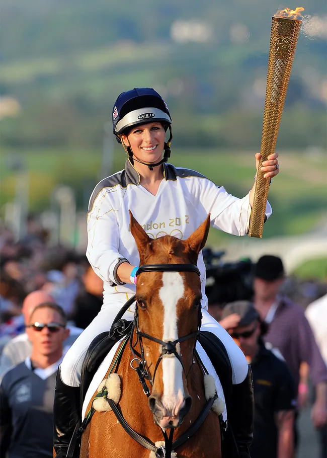 Rider carrying the Olympic torch on horseback during the London 2012 relay event, wearing a helmet and uniform.
