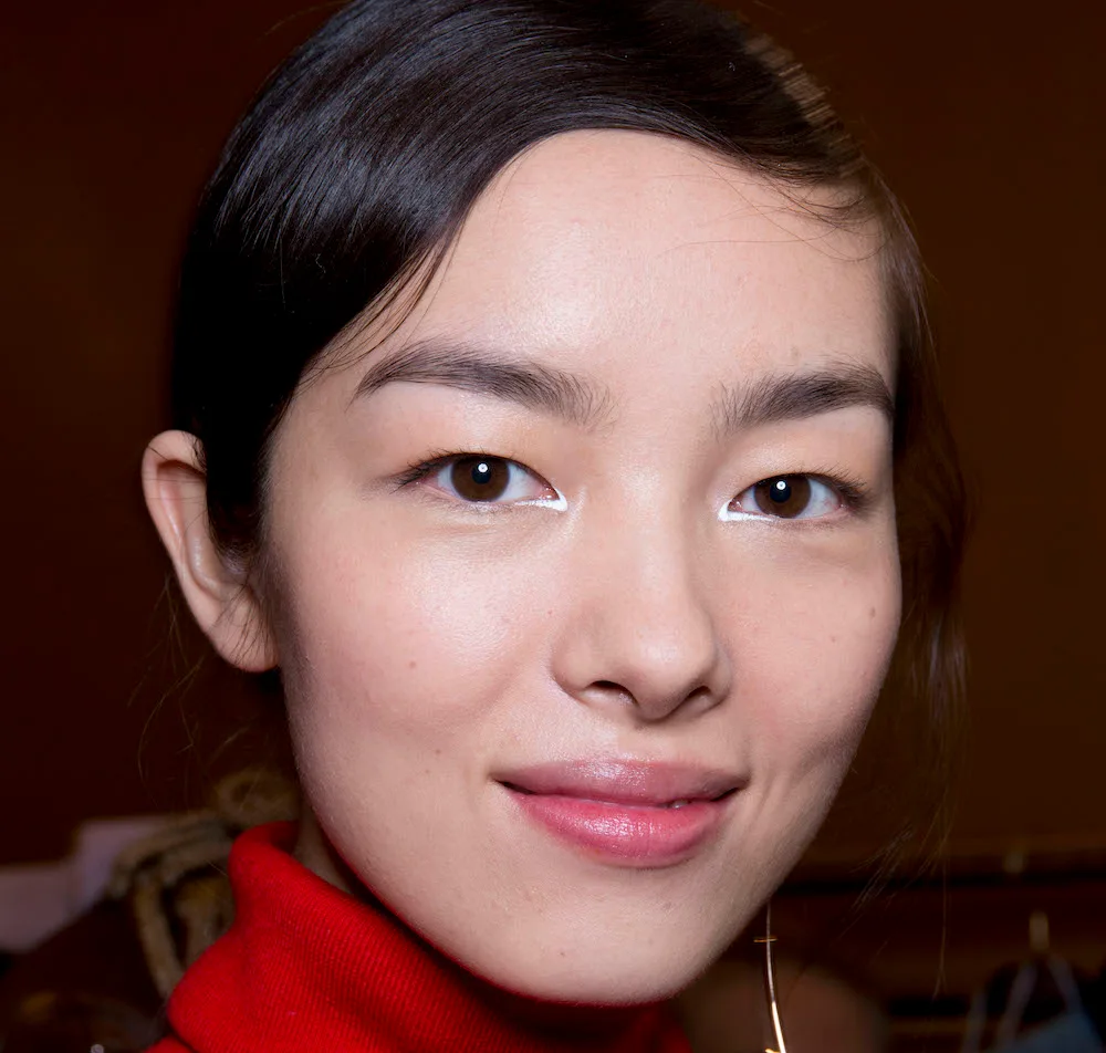 ```
Close-up of a woman with a neutral expression, wearing a red top, and white eyeliner highlighting her eyes.
```