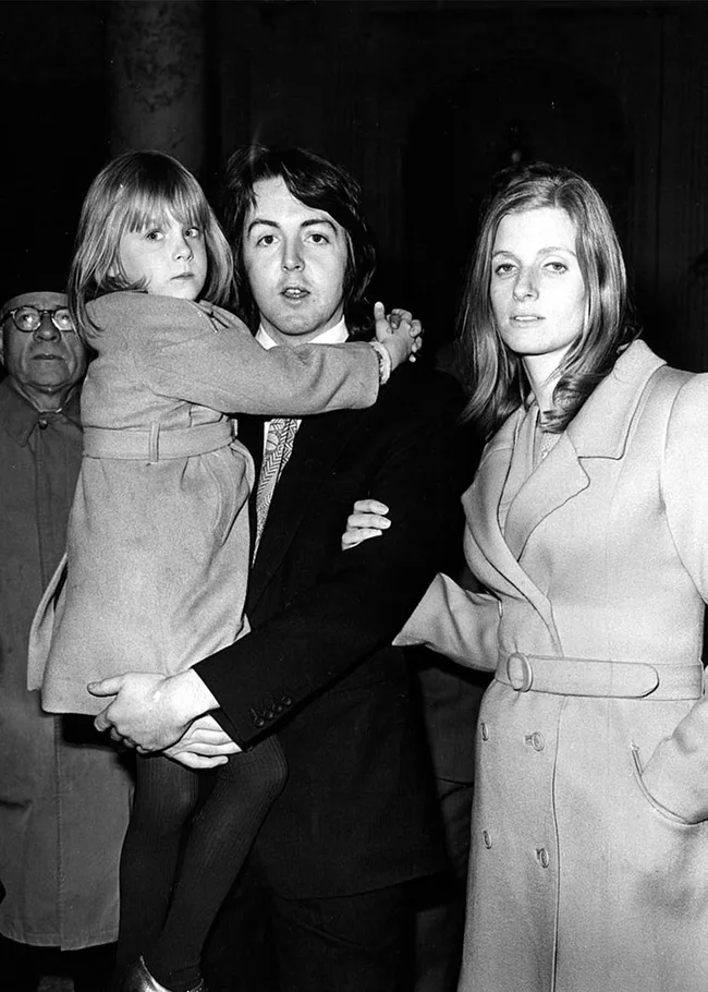 A man holds a child, with a woman standing beside them, all wearing coats and looking at the camera. Black and white photo.