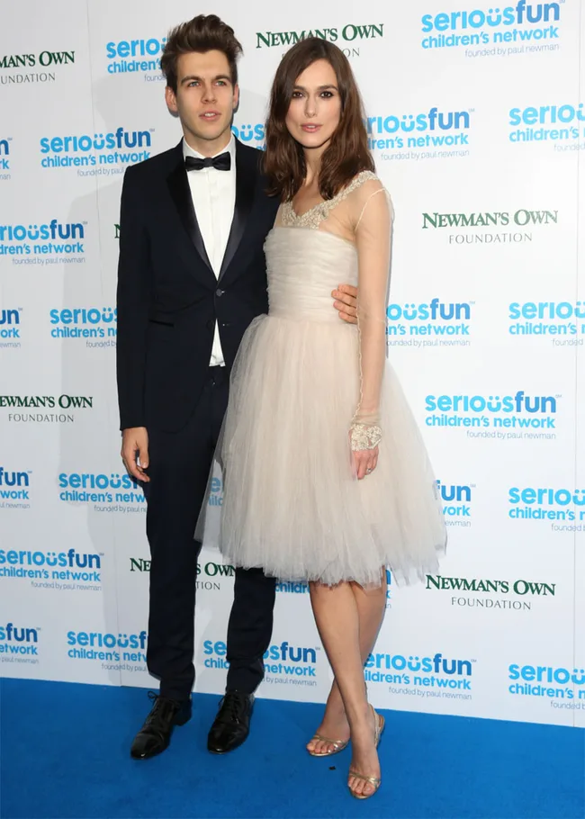 Man in black suit and woman in white dress on blue carpet at SeriousFun Children's Network event.