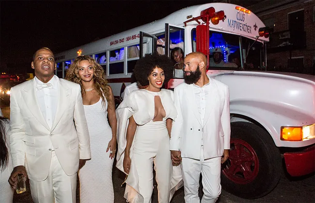 Group of people in white outfits walking at night beside a decorated party bus labeled "Club Mayweather."