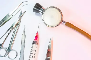 Medical tools including a stethoscope, syringe, scissors, and tweezers arranged on a white surface.