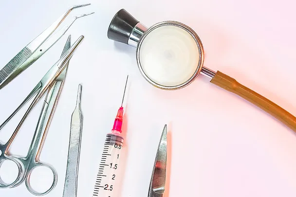 Medical tools including a stethoscope, syringe, scissors, and tweezers arranged on a white surface.