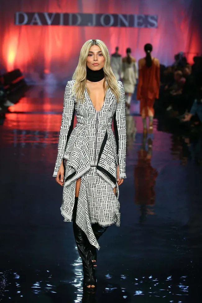 Model in black and white patterned dress, black boots, walking on runway with "David Jones" banner.