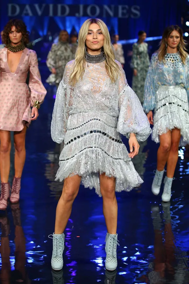 Fashion show with models in glittery dresses and boots, walking down a glossy runway with "David Jones" in the background.