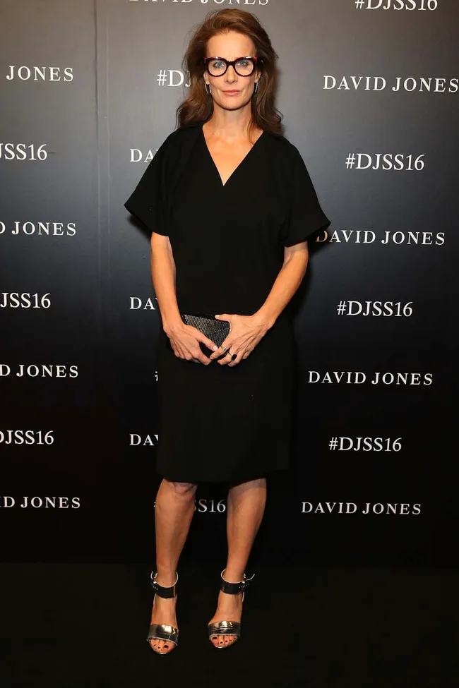 Woman in black dress and glasses at a David Jones event backdrop, labeled #DJSS16.