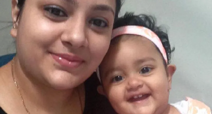 A woman smiles with a baby girl wearing a peach headband, both appearing happy and close together.