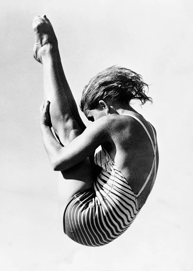 Diver in a striped swimsuit performing a pike dive against a clear sky.