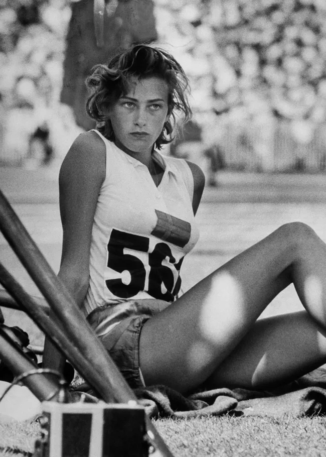 Young athlete sitting on grass, wearing a numbered sports jersey, during a sporting event. Black and white photo.