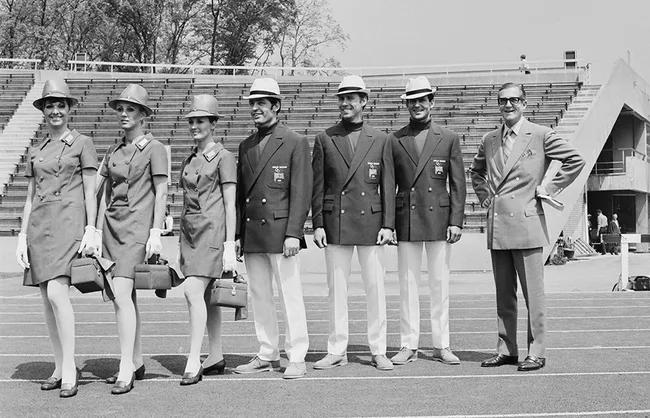 Group of people in matching uniforms and hats posing on a track in a stadium setting.