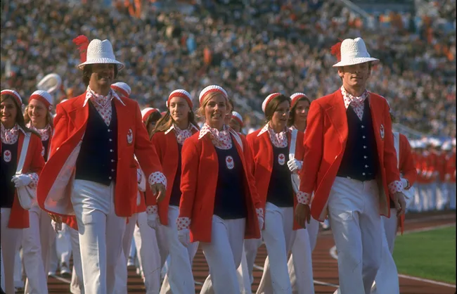 Canadian Olympic team in red blazers and white hats marching in a stadium during the 1976 Games opening ceremony.