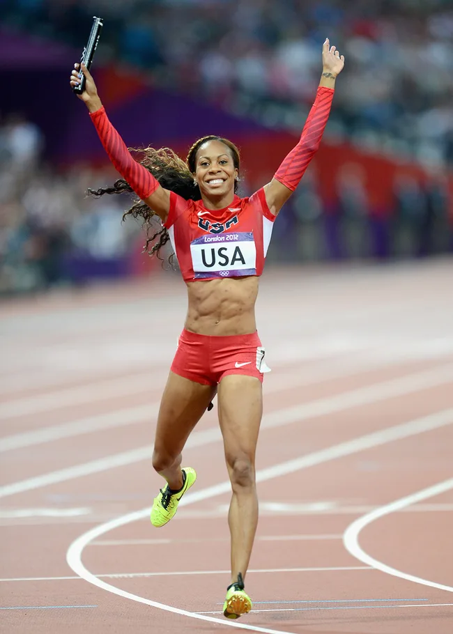 Athlete in red USA uniform celebrates with baton on a track, arms raised, at the London 2012 Olympics.