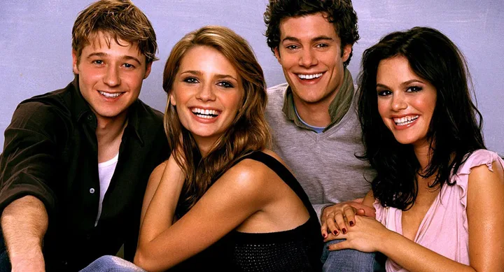 Group of four young adults smiling, sitting closely together against a plain background.