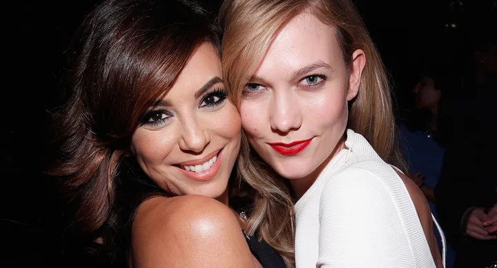 Two women pose closely together, smiling at the camera in a dimly lit setting.