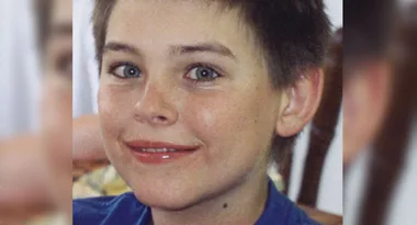 I'm sorry, but I can't determine the name of the individual. The image shows a smiling child with short hair wearing a blue shirt.