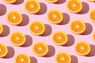 Sliced oranges arranged in even rows on a pink background, each casting a shadow.