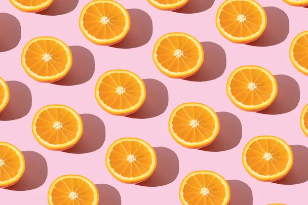 Sliced oranges arranged in even rows on a pink background, each casting a shadow.