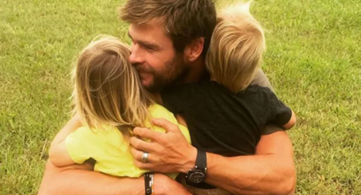 Man hugging two children on a grassy field.