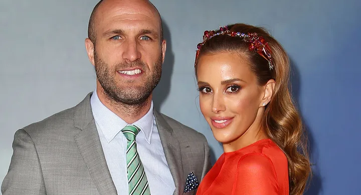 Man in suit and tie with woman in red dress and jeweled headband, both smiling at a formal event.