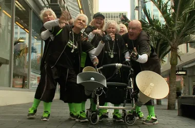 Group of elderly people wearing matching outfits and sneakers, posing energetically on a city street with a stroller and megaphone.