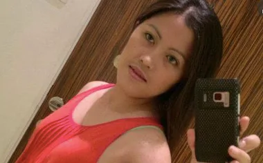 Selfie of a woman in a red top, holding a phone with a black case, taking a mirror photo.