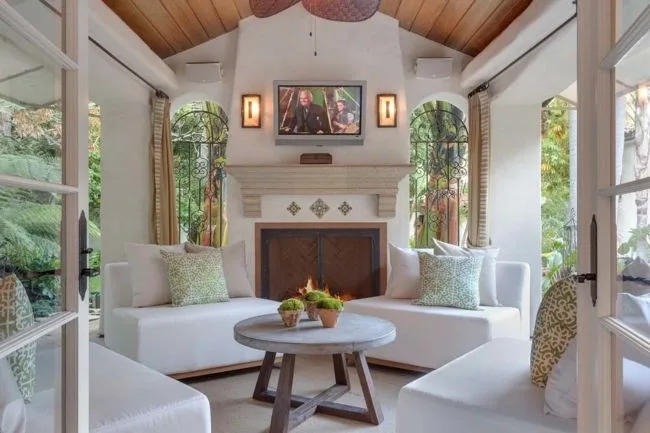 Luxurious outdoor living room with a fireplace, elegant furniture, and a TV above the mantel showing a movie scene.