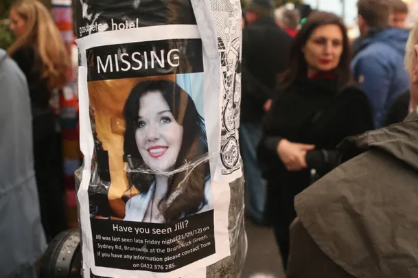 A missing person poster for "Jill" on a pole in a crowded area, with a woman's photo and details about her disappearance.