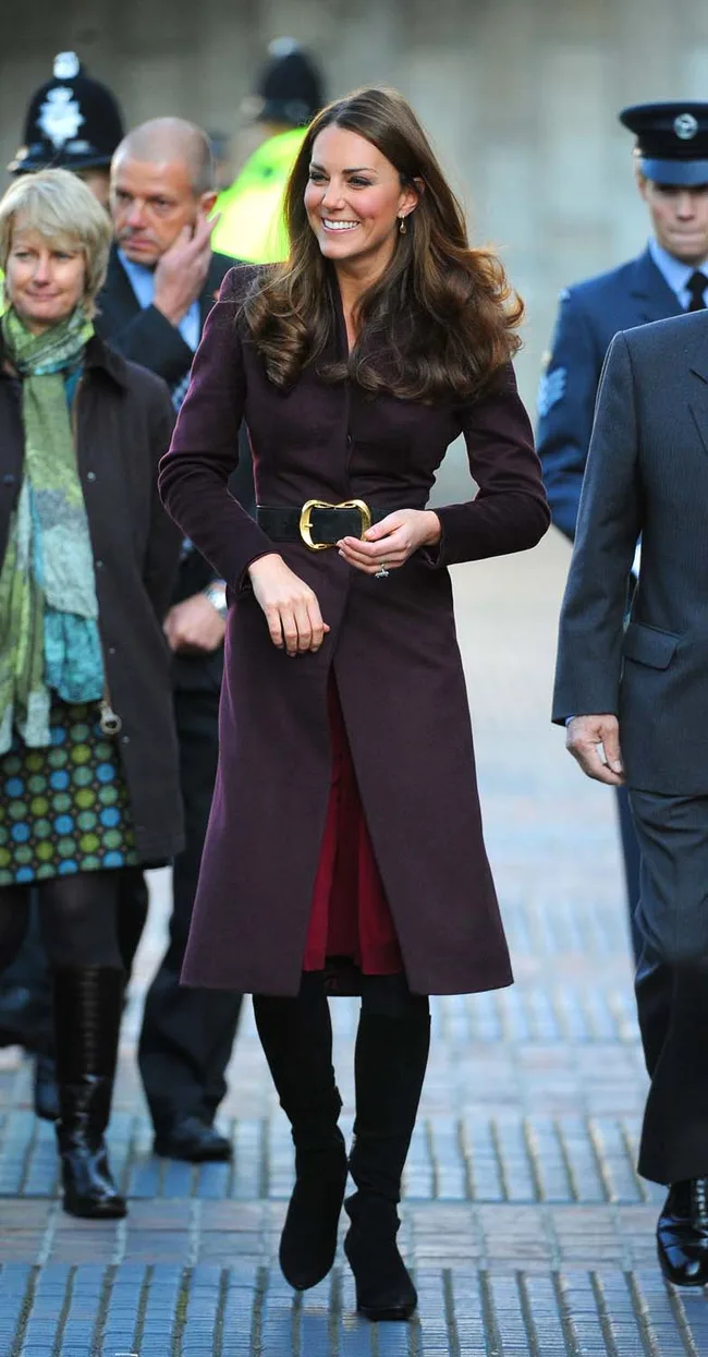 A woman in a long coat and boots walking outside with several people around her.