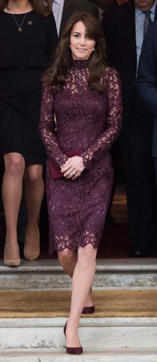 Woman in a burgundy lace dress, holding a clutch, descending steps surrounded by people.