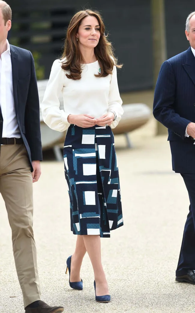 Woman in white blouse and geometric skirt walking with two men in suits on a path.
