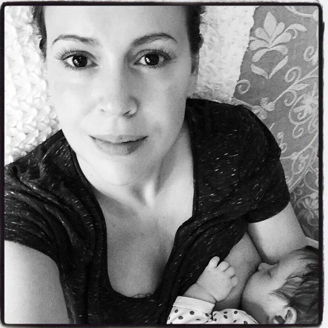 Woman breastfeeding a baby, lying on a patterned pillow, captured in a black and white photograph.