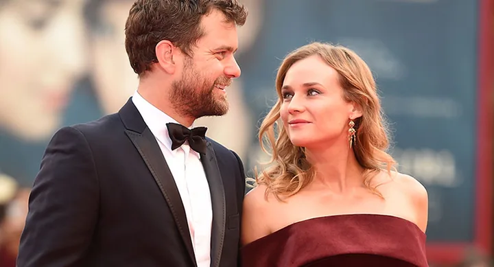 Man in tuxedo smiling at woman in burgundy gown on red carpet.