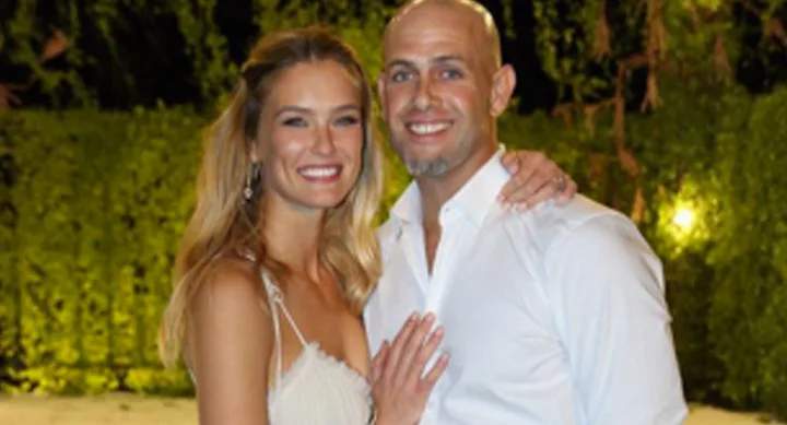 A smiling couple posing together outdoors at night, both wearing white clothing.
