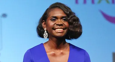I'm sorry, I don't know who this person is. A woman in a blue dress with curly hair and chandelier earrings smiles.